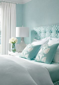 a bedroom with blue walls and white bedding in front of a large window that looks out onto the water