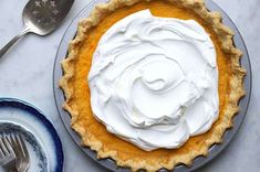 a pie with whipped cream on top sitting next to a fork and spoon, along with another pie in the background