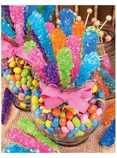 colorful candies are in a glass bowl on a table next to candy sticks and lollipops