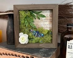 an old book with moss and flowers in it on a shelf next to some bottles