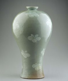 a green vase with white flowers on the top and bottom, sitting in front of a gray background