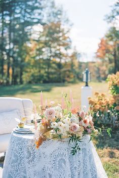 a table with flowers and candles on it in the middle of a field near a couch