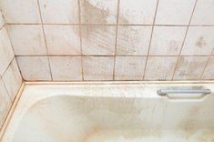 a dirty bathtub in the corner of a tiled bathroom with no shower curtain on it