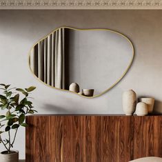 a mirror on the wall above a wooden cabinet with vases and potted plant