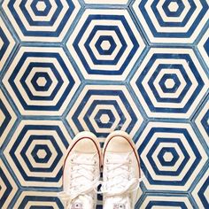 a pair of white tennis shoes standing in front of a blue and white wallpaper