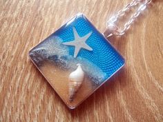 a glass tile necklace with a starfish and sea shell on the bottom, sitting on a wooden surface