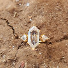 a diamond ring sitting on top of a dirt ground next to a stone wall with two diamonds