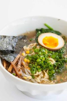 a white bowl filled with soup and vegetables on top of a table next to an egg