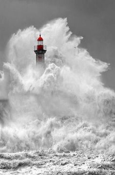 a lighthouse in the middle of a large wave with it's red light on