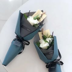 three flowers are wrapped in blue paper and tied with black ribbon on a white table