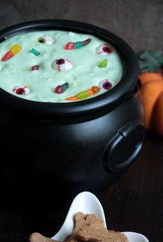 a black pot filled with green liquid next to a bowl of dog food and two small orange pumpkins