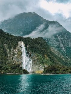 a large waterfall in the middle of a body of water with mountains in the background