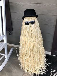 a fake long haired man with sunglasses and a hat on the front door steps to a house