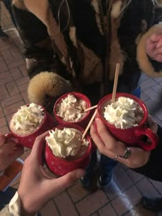 four people holding red mugs filled with whipped cream