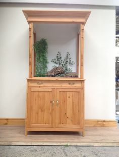 a wooden cabinet with plants in it sitting on top of a hard wood floor next to a white wall