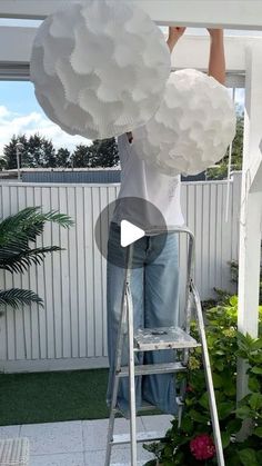 a woman standing on a stepladder holding giant white paper clouds over her head