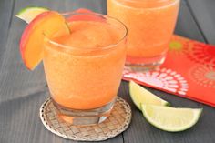 two glasses filled with orange juice and garnished with limes on a table