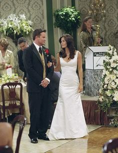 a man and woman standing next to each other in front of a table with flowers