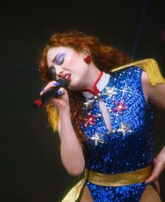 a woman with red hair wearing a blue dress and holding a microphone in her right hand