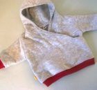 a child's hoodie with red trim on the sleeves and bottom, sitting on a white surface