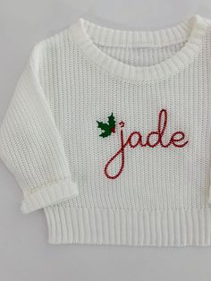 a white sweater with the word jade written on it and a green leaf in red