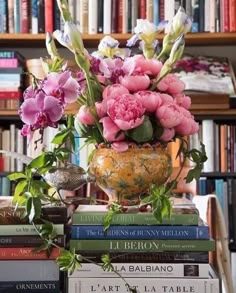 a vase filled with pink flowers sitting on top of a pile of books