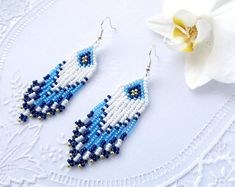 a pair of blue and white beaded earrings on a lace doily next to a flower