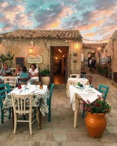 several people sitting at tables in front of a building with potted plants on it