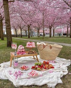 a picnic with food and drinks on the grass in front of cherry blossom covered trees