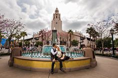 a man and woman sitting on a fountain in front of a building with a clock tower