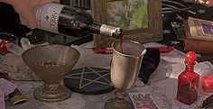 a person pouring red wine into two silver goblets on a table with other items