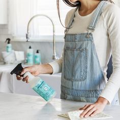 a woman in an apron is cleaning the counter top with a rag and bottle of soap