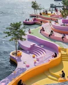 people are sitting and standing on colorful benches by the water