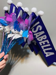 a person holding up a purple and blue bouquet with white pom poms on it