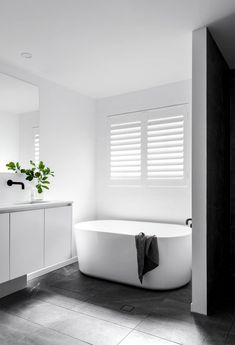 a white bath tub sitting in a bathroom next to a sink and window with shutters