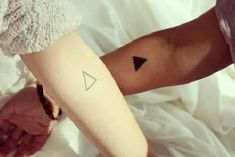 two people holding hands with tattoos on their arms and one has a small black triangle