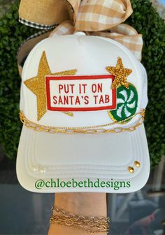 a white hat with gold stars and a sign that says put it on santa's tab