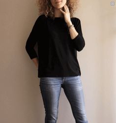 a woman standing in front of a white wall with her hand on her chin and looking at the camera