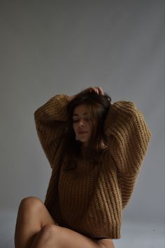 a woman is sitting on the floor with her legs crossed and wearing a brown sweater