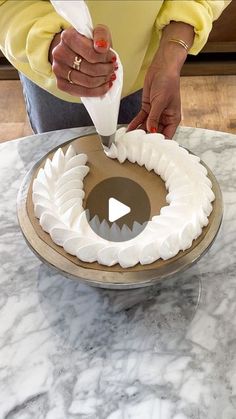 a woman is decorating a cake with white icing on a marble table top