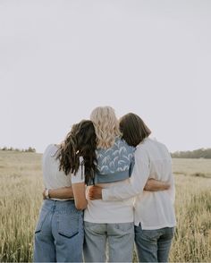 three women standing in a field with their arms around each other looking at the sky