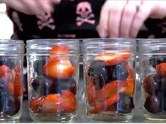 several jars filled with oranges and blackberries on a table next to a woman's hand