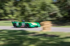 a green race car driving down a road with trees in the backgrouund