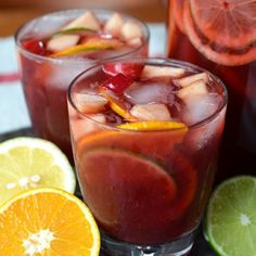 two glasses filled with fruit and ice next to sliced oranges