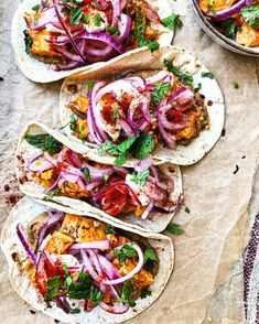 three tacos with meat, onions and tomatoes on top are sitting on parchment paper