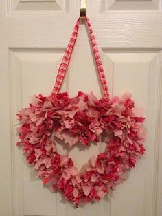 a heart shaped wreath hanging on the front door with pink tissue paper flowers in it