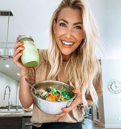 a smiling woman holding a bowl of food and a green smoothie in her hand