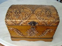 an ornate wooden box sitting on top of a white tablecloth covered round table with chairs in the background