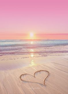 a heart drawn in the sand on a beach at sunset with waves coming in from the ocean