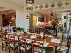 a dining room table with many chairs and plates on the wall above it, in front of an open kitchen